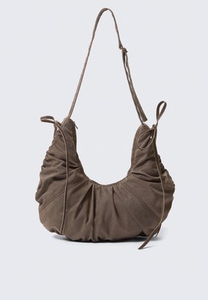 Braune Wildleder-Schultertasche mit gerafften Details, verstellbarem Träger und dekorativen seitlichen Bändern, vor neutralem Hintergrund dargestellt.