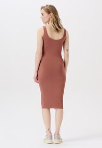 Rostfärgad ribbad klänning med en figurnära silhuett och kjol som slutar vid låren. Har breda axelremmar och en rundad ryggdesign.