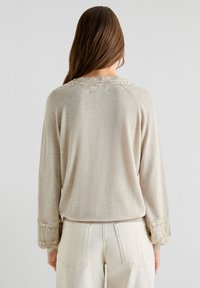 Maglione beige con maniche lunghe, caratterizzato da un motivo a maglia testurizzato, bordi in pizzo ai polsini e un delicato dettaglio in pizzo attorno al collo.