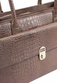 Bruine tas van krokodillenleer met reliëf, dubbele handvatten, een ritsvak en een gouden sluitingdetail aan de voorkant.