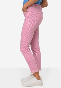 Roze en witte gestreepte broek met een getailleerde pasvorm, voorzien van een hoge taille en zijzakken. Gecombineerd met witte sneakers.