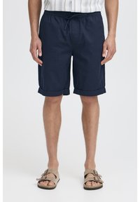 Marineblå bomuldsshorts med elastisk talje, snøre og opbrettede kanter, kombineret med beige sandaler med to justerbare remme.