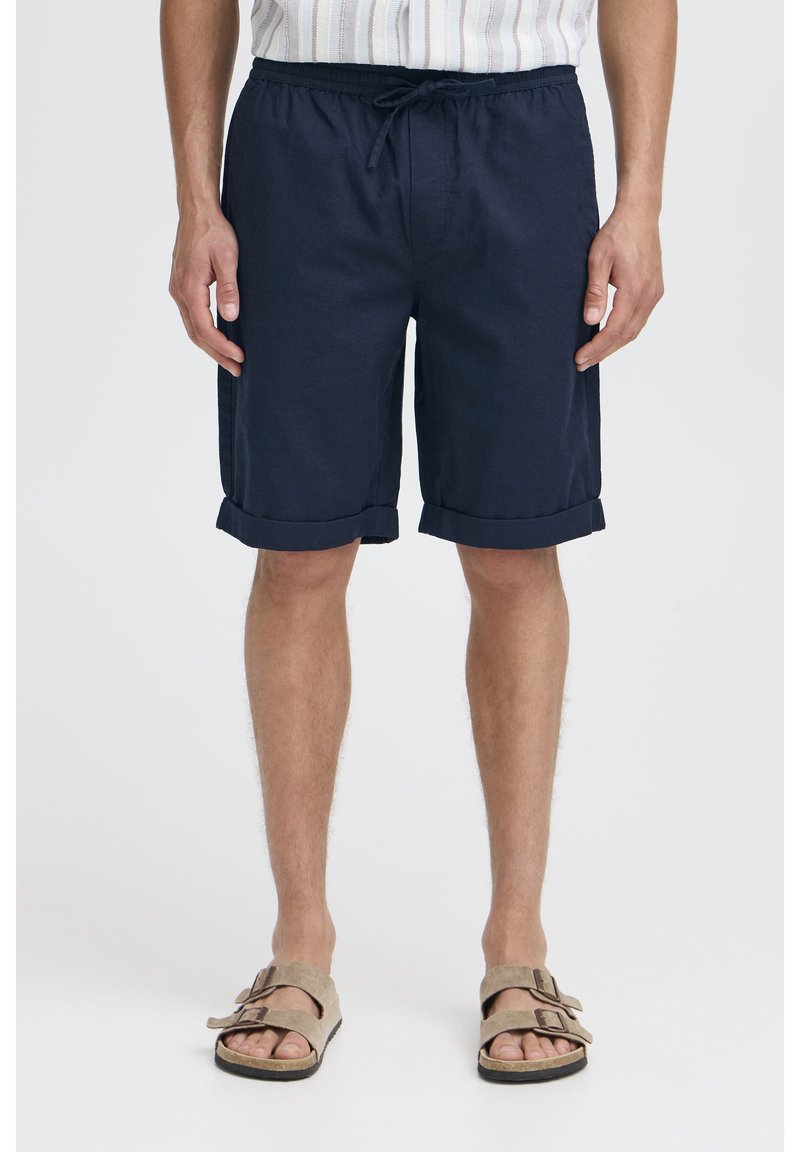 Marineblå bomuldsshorts med elastisk talje, snøre og opbrettede kanter, kombineret med beige sandaler med to justerbare remme.