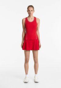 Rode sportieve tanktop met witte accenten en een aansluitend ontwerp, gecombineerd met een bijpassende flared rok; gedragen met witte sneakers.