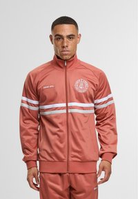 Zip-up trackjakke i støvet rose med hvide striber, ribbede manchetter og et logo-patch på brystet. Lavet af glat, letvægtsstof.