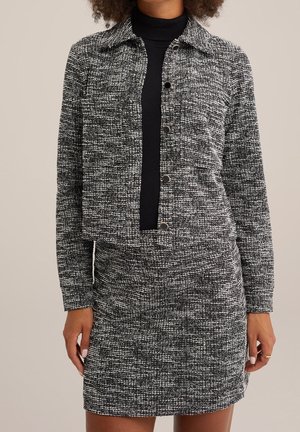 Giacca tweed bianca e nera con colletto e chiusura a bottoni, abbinata a una gonna coordinata. Entrambi i pezzi presentano un motivo tessuto testurizzato.