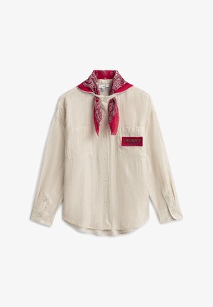 Chemise beige à boutons avec deux poches poitrine, un écusson rouge marqué "True North" et un bandana rouge à motifs noué autour du col.
