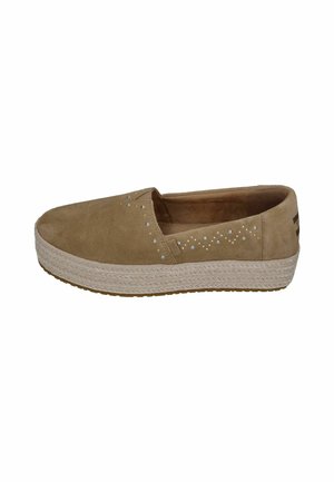 Beiger Slip-On-Schuh mit Plateausohle und kleinen dekorativen Nieten, die auf der Seite ein Wellenmuster bilden.