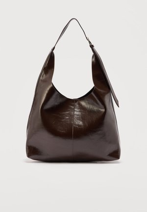 Ciemnobrązowa błyszcząca skórzana torebka na ramię z pojedynczym szerokim paskiem i klamrą po jednej stronie, na jasnym, jednolitym tle.