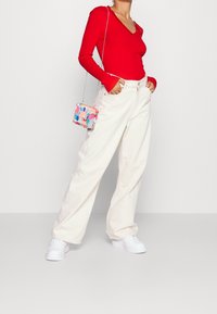 Punainen pitkähihaisellinen ribbipaita, kermaväriset leveälahkeiset housut, valkoiset lenkkarit ja monivärinen pilkullinen minilaukku, jossa on hopeanvärinen ketjuhihna.