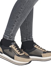 Sneakers beige e neri con pannelli in mesh, chiusura con lacci, cerniera laterale e superfici testurizzate. Indossati con jeans skinny grigi.