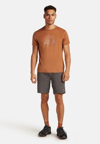 Kurzärmliges braunes Hemd mit weißem Grafikdesign, kombiniert mit grauen Shorts und schwarzen Sneakers mit bunten Akzenten.