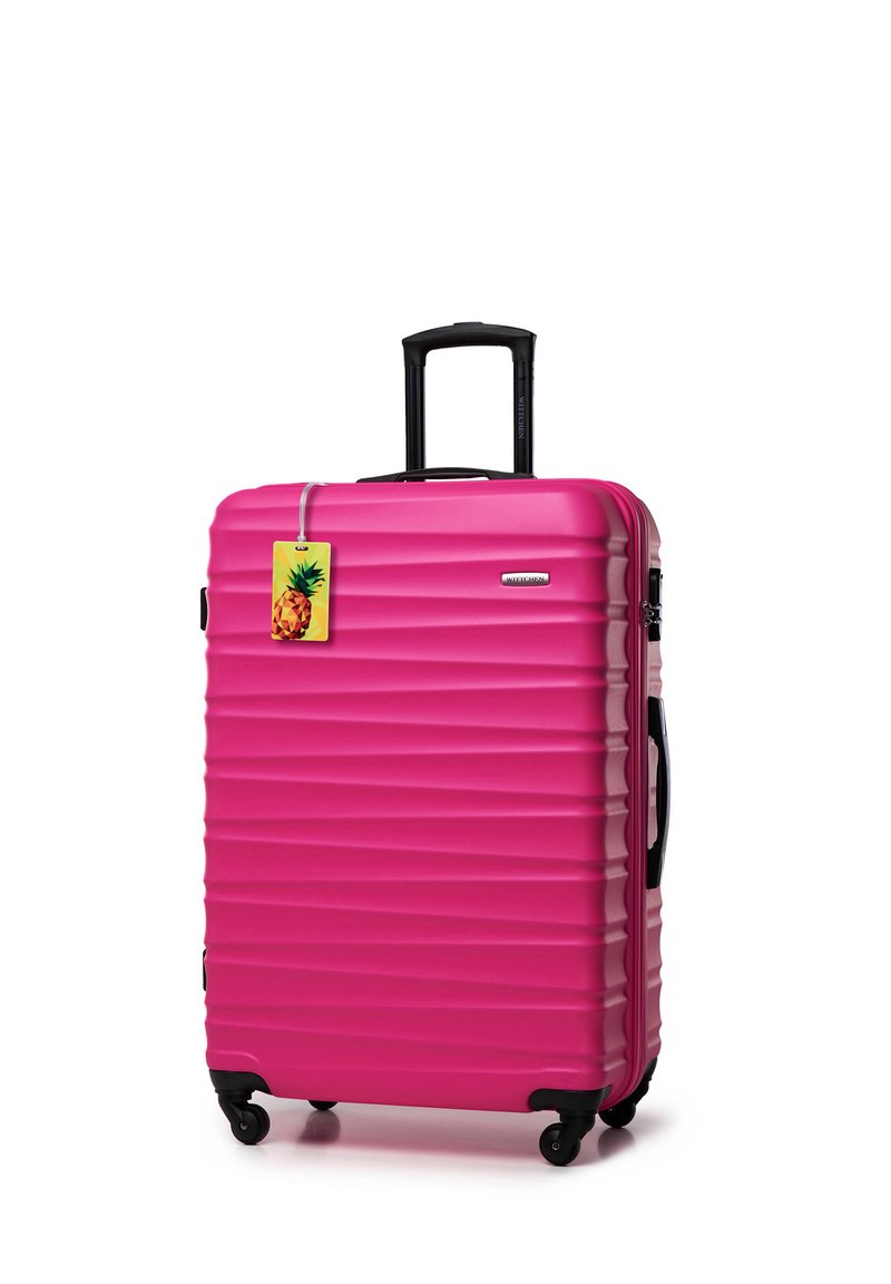 Valise rigide rose avec des rainures horizontales, poignée rétractable noire, roues et une étiquette de bagage en forme d'ananas attachée.