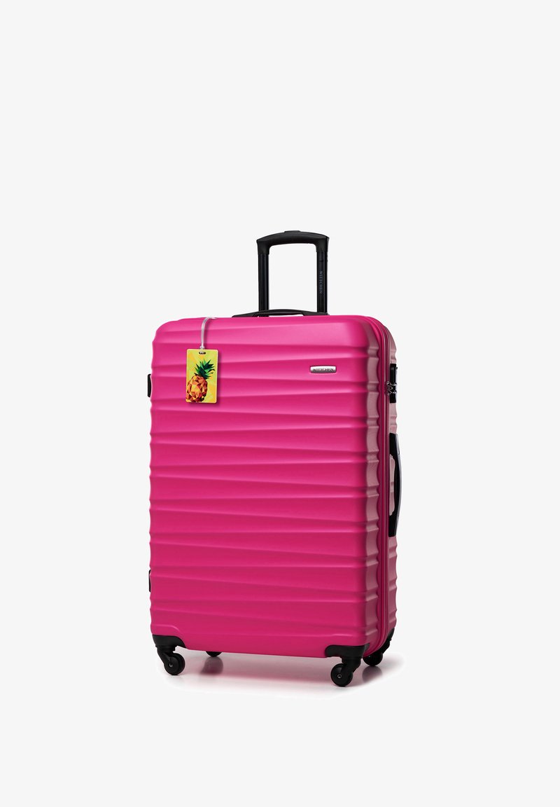 Valigia rigida rosa con righe orizzontali, manico nero retrattile, ruote e un'etichetta per bagagli a forma di ananas attaccata.
