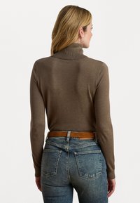 Suéter castanho de gola alta com uma textura suave, design ajustado e mangas longas, combinado com jeans de cintura alta, azul desbotado e um cinto bege.