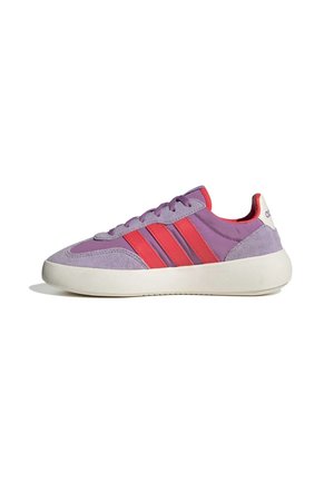 Zapatilla deportiva morada con rayas rojas, parte superior de ante y tela, suela blanca gruesa y diseño de tobillo bajo, mostrada de lado sobre un fondo blanco.