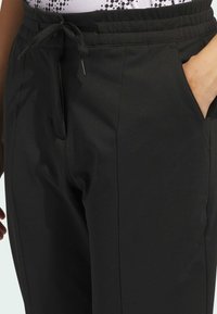 Svarta jogger-byxor av slät tyg, med dragsko i midjan, sidofickor och avslappnad passform. Minimalistisk design utan märkbara mönster.