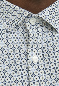 Maglietta a maniche corte con un motivo geometrico blu e crema, caratterizzata da un bottone bianco al colletto e un dettaglio in tessuto testurizzato.