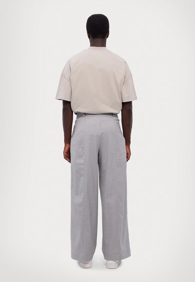 Light gray wide-leg trousers with a high waist and subtle front pleats, paired with a short-sleeved beige shirt. White sneakers complete the look.