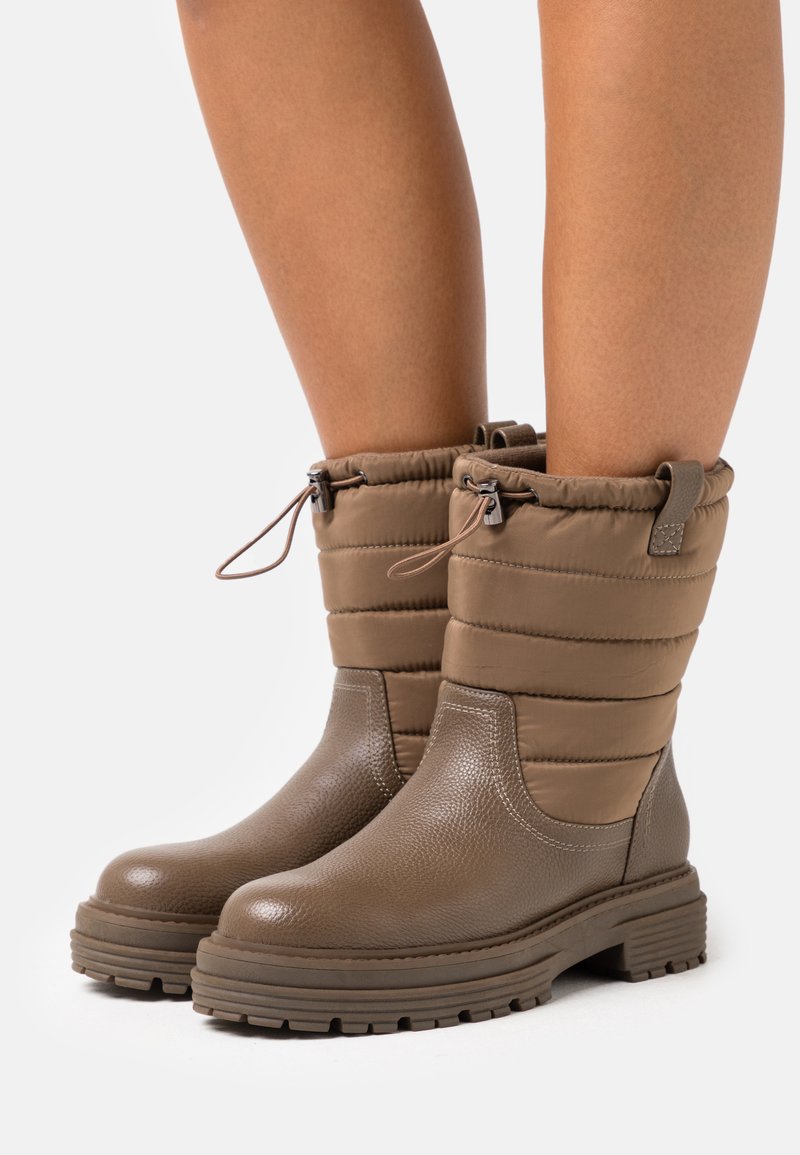 Bottines imperméables brun avec une partie inférieure en cuir texturé et une partie supérieure en nylon matelassé, dotées d'une fermeture à cordon et d'une semelle épaisse.