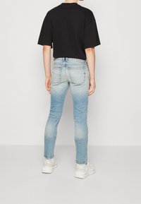 Svart oversized t-shirt, ljusblå smal passform jeans, med medelblå tvätt och blekningar. Vita sneakers med tjock sula. Inga synliga mönster eller detaljer.