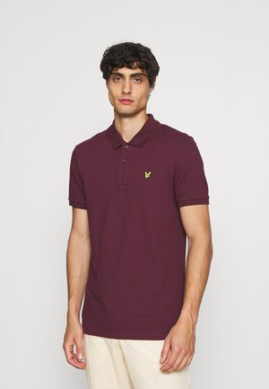 Polo en bordeaux en coton, avec un col à trois boutons, des manches courtes et un petit logo jaune sur la poitrine gauche.