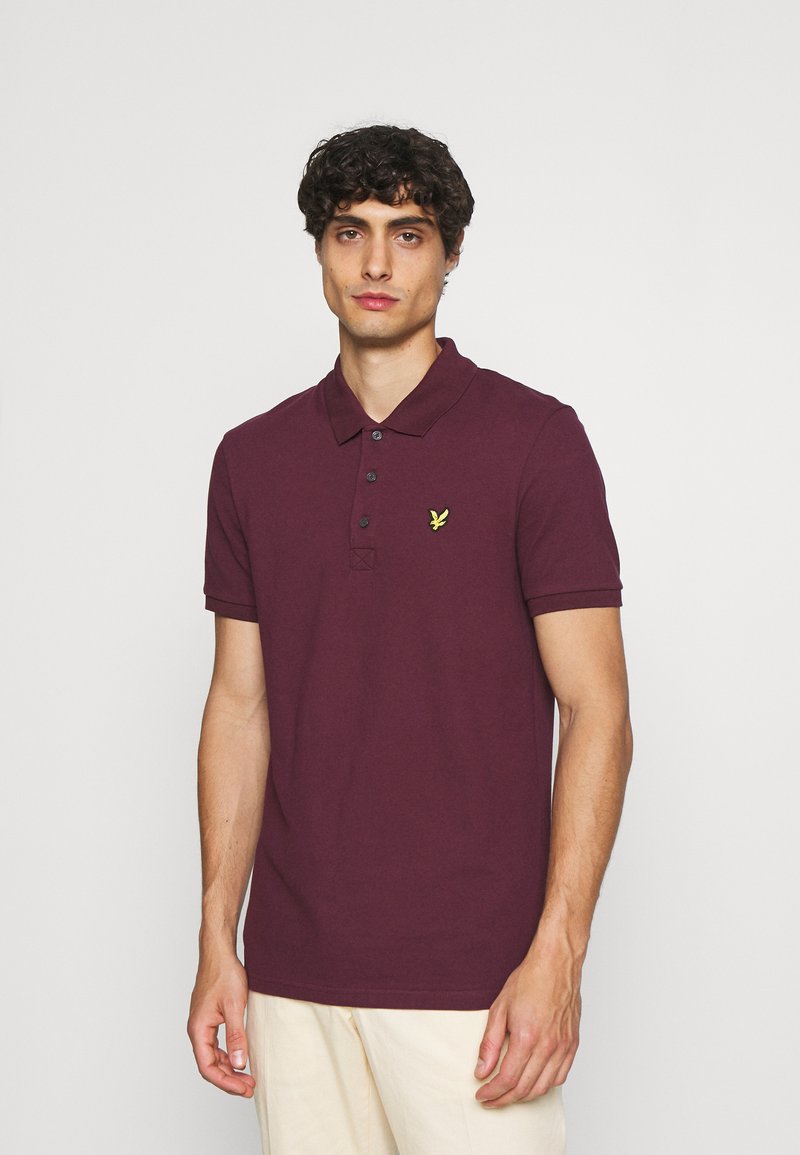 Burgundská polo košile vyrobená z bavlny, má přední zapínání na tři knoflíky, krátké rukávy a malé žluté logo na levém prsu.