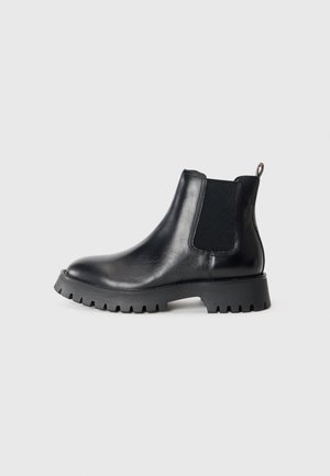 Black leather Chelsea boot with elastic side panel, pull tab at the back, and rugged lug sole for traction on a plain background.