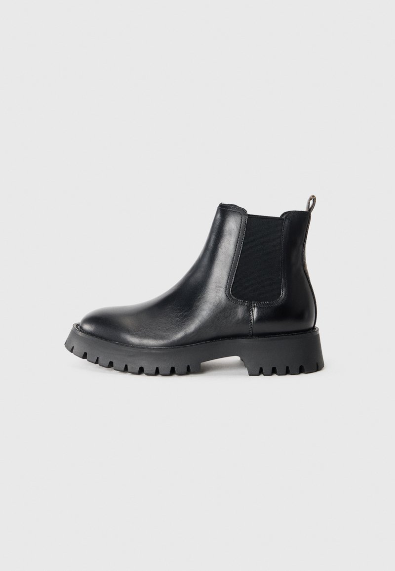 Botte Chelsea en cuir noir avec panneau élastique sur les côtés, languette à l'arrière et semelle crantée pour une adhérence, sur fond uni.