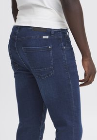 Donkerblauwe spijkerbroek met een slim fit, met een vervaagde textuur, standaard achterzakken en een zwarte leren patch op de tailleband.