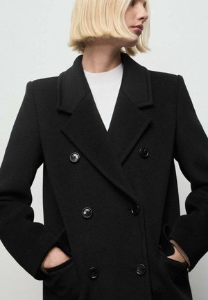 Cappotto doppio petto nero con rever a punta, grandi bottoni neri e tasche laterali. Realizzato in tessuto di lana testurizzato.
