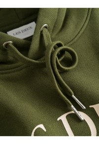 Felpa verde con un tessuto texturizzato, dotata di cappuccio e cordino. Etichetta 'LES DEUX' visibile nella zona del collo.