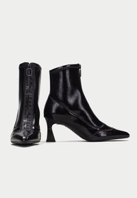 Stivali alla caviglia in pelle verniciata nera con punta affusolata, zip laterali e tacco a blocco di media altezza. Presentano dettagli di cuciture testurizzate.