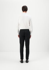 Camisa blanca de manga larga con puños abotonados, combinada con pantalones negros ajustados que tienen cinturilla. El modelo lleva zapatos negros.