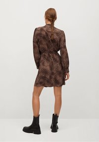 Robe marron à imprimé léopard avec manches longues et taille ceinturée. Le tissu semble léger. Portée avec des bottines noires.