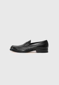 Zwarte leren loafers met een ronde neus, contrasterende stiksels en een lage hak, met een decoratieve band over de voorkant. Gladde textuur.