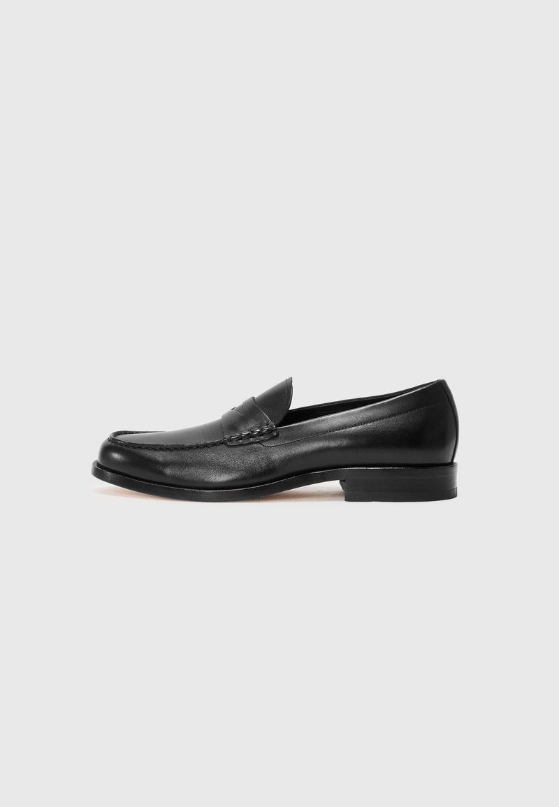 Zwarte leren loafers met een ronde neus, contrasterende stiksels en een lage hak, met een decoratieve band over de voorkant. Gladde textuur.