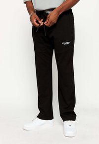 Sorte sweatpants lavet af blød stof, med en elastisk talje med snoretræk og et sidelogo i hvid. Enkel design.
