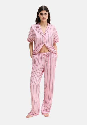 Woman wearing pink and red vertical striped short-sleeve button-up shirt and matching drawstring pants, standing barefoot on white background.