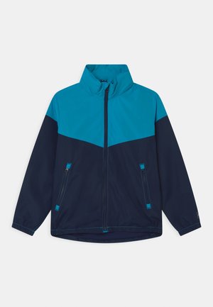 Vindjakke med en turkise overdel og marineblå nederdel. Har en høj krave, lynlås-lommer og kontrasterende syninger.