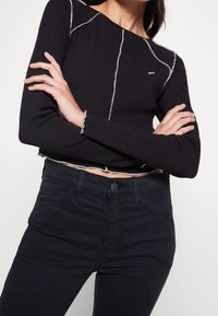 Svart ribbad långärmad topp med vit kontrasterande sömnad och rå kant, i kombination med mörka slim-fit byxor med knappstängning.