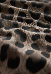 Tissu en léopard avec une surface texturée, présentant de grandes taches noires sur un fond marron clair, disposées dans un motif fluide.