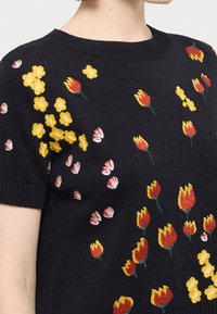 Suéter negro de punto con mangas cortas, con vibrantes flores amarillas y tulipanes rojos bordados en la parte delantera en tamaños variados.
