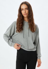 Sudadera holgada de color gris claro con cordón, mangas largas y dobladillo acanalado, combinada con leggings ajustados negros. Textura de tela suave.