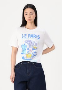 Valkoinen puuvillainen t-paita, jossa on sininen ja vaaleanpunainen graafika kahvipannusta, kukista ja aamiaisruuista, sekä tekstit "LE PARIS" ja "BREAKFAST CLUB."