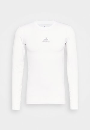 T-shirt de sport à manches longues, blanc, fabriqué en tissu lisse et extensible. Il présente un logo Adidas gris sur la poitrine et un col rond.