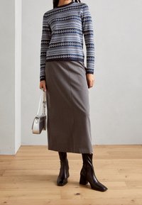 Pull en tricot bleu marine à motifs géométriques, jupe crayon grise, bottines noires à bout carré, et sac à épaule métallique.