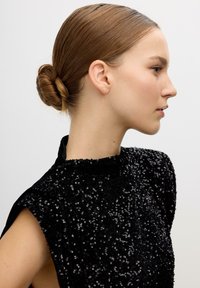 Vestido negro con lentejuelas, de cuello alto y sin mangas, visto de lado; cabello recogido en un moño ordenado.