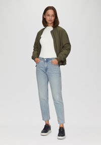 Kurtka typu bomber w ciemnozielonym kolorze, tekstura prążkowana; biały top prążkowany; jasnoniebieskie dżinsy; granatowe sneakersy z białymi podeszwami; luźny krój.