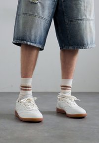 Hvite sneakers med gummisåler, parret med hvite og brune stripete sokker, og blå denimshorts med slitte detaljer.
